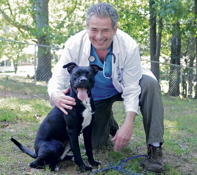 A man kneeling down next to a black and white dog.